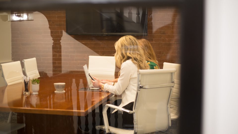 Two people reviewing a tablet at a conference table in a brick-walled meeting room