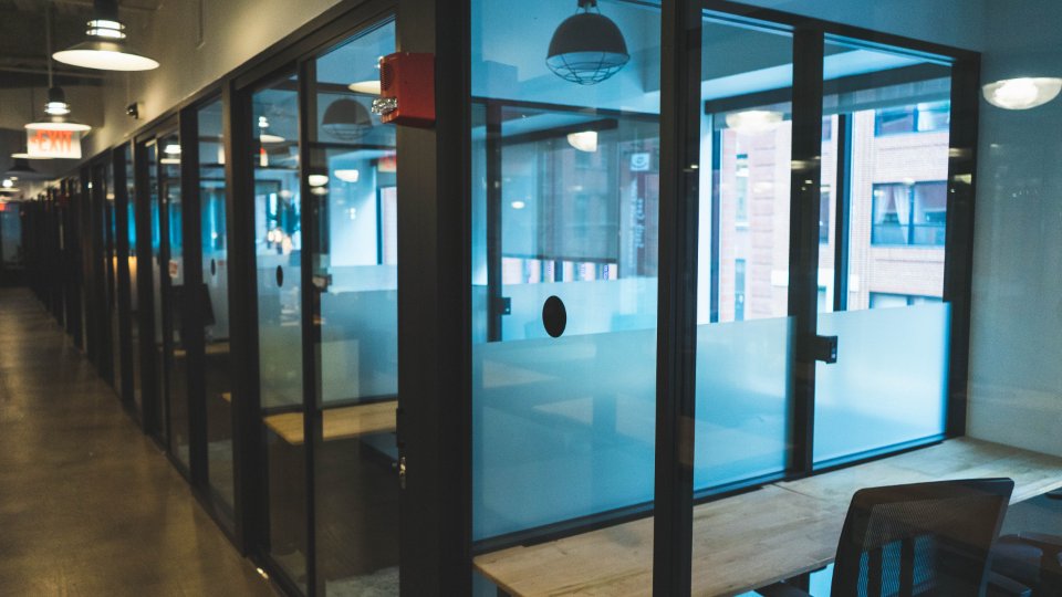 Row of glass-walled breakout rooms along a corridor in a converted loft building