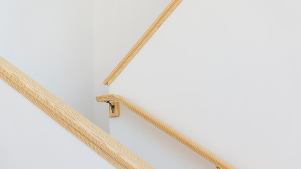 Escalier intérieur aux murs blancs avec main courante continue en bois fixée au mur